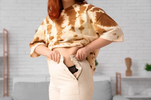 Image of woman trying to do her trousers up after pregnancy weight gain Bracknell