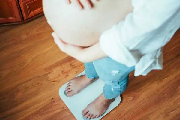 Image of woman weighing herself and experiencing weight gain through pregnancy Bracknell